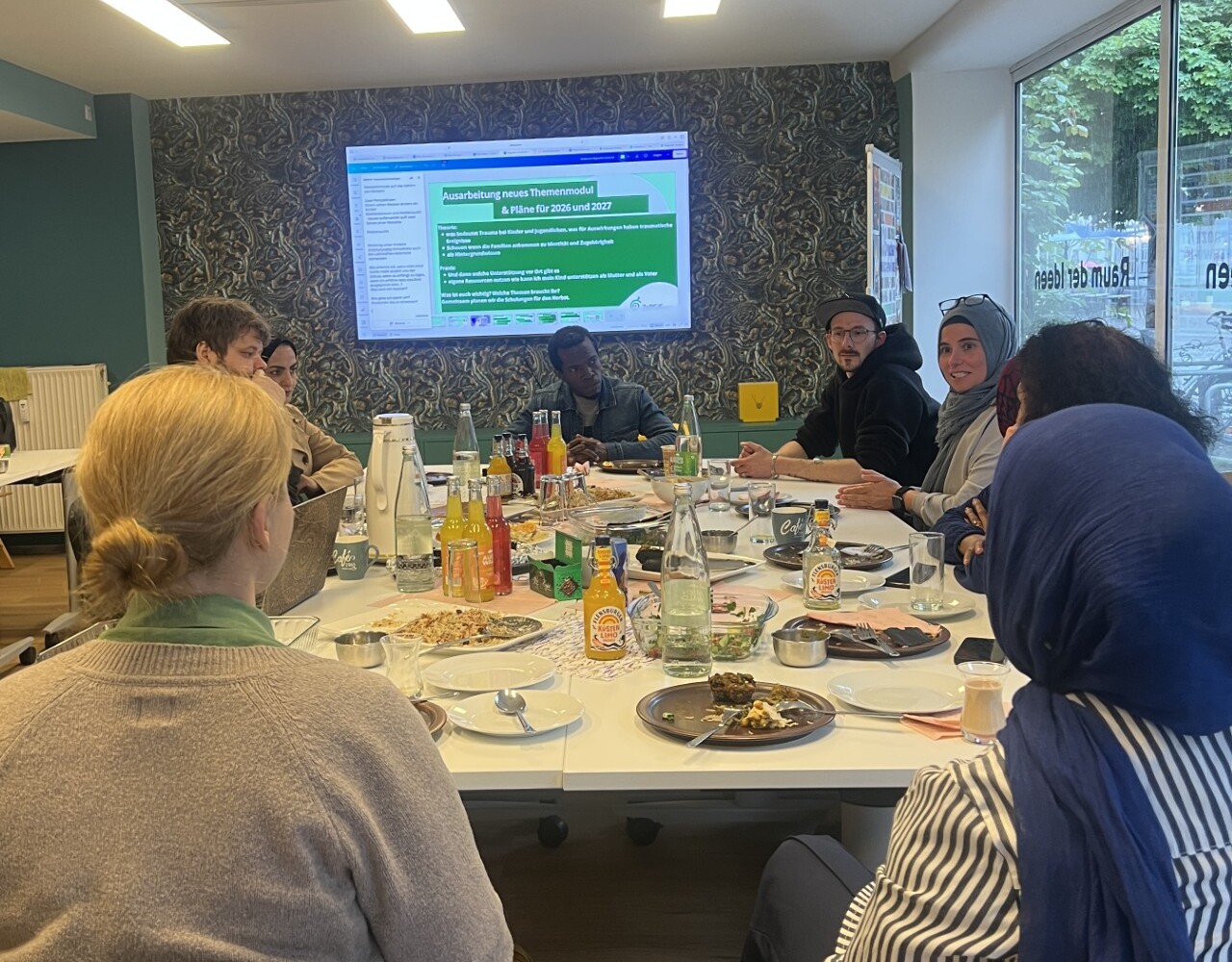 Mitarbeiter des Projekts sitzen an einem großen Tisch und schauen auf einen Smartscreen